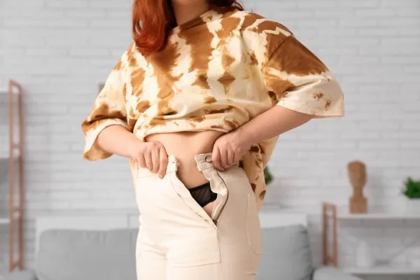 Image of woman trying to do her trousers up after pregnancy weight gain Gorgie